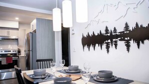 Una cocina moderna con electrodomésticos de acero inoxidable, un comedor con mesa lista para cuatro personas, y una lámpara de pared.