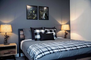 A bedroom with a bed, two wall-mounted picture frames, two bedside lamps, a nightstand, and a decorative deer figurine. - Absolutely Revy - Ground Level Condo with Hot Tub (Revelstoke)