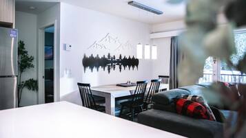 A modern living room with a dining area, a sofa, and a wall-mounted artwork of mountains.