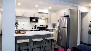 Una cocina moderna con una isla central, electrodomésticos de acero inoxidable y taburetes de bar.