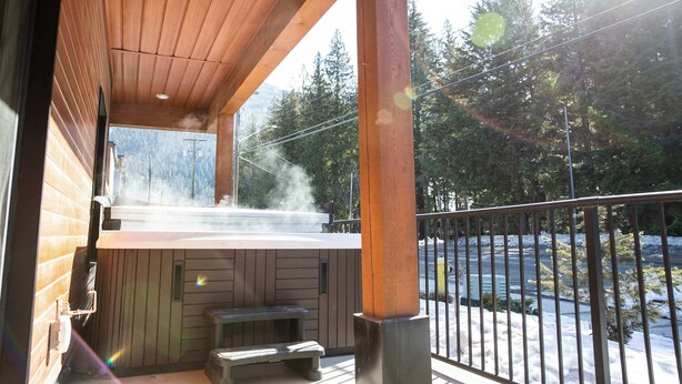 Una terraza de madera con un jacuzzi, bancos y vistas a un paisaje nevado.
