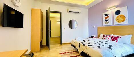 Ein modernes Hotelzimmer mit Bett, Schreibtisch, Fernseher und einer Tür zu einem weiteren Raum.