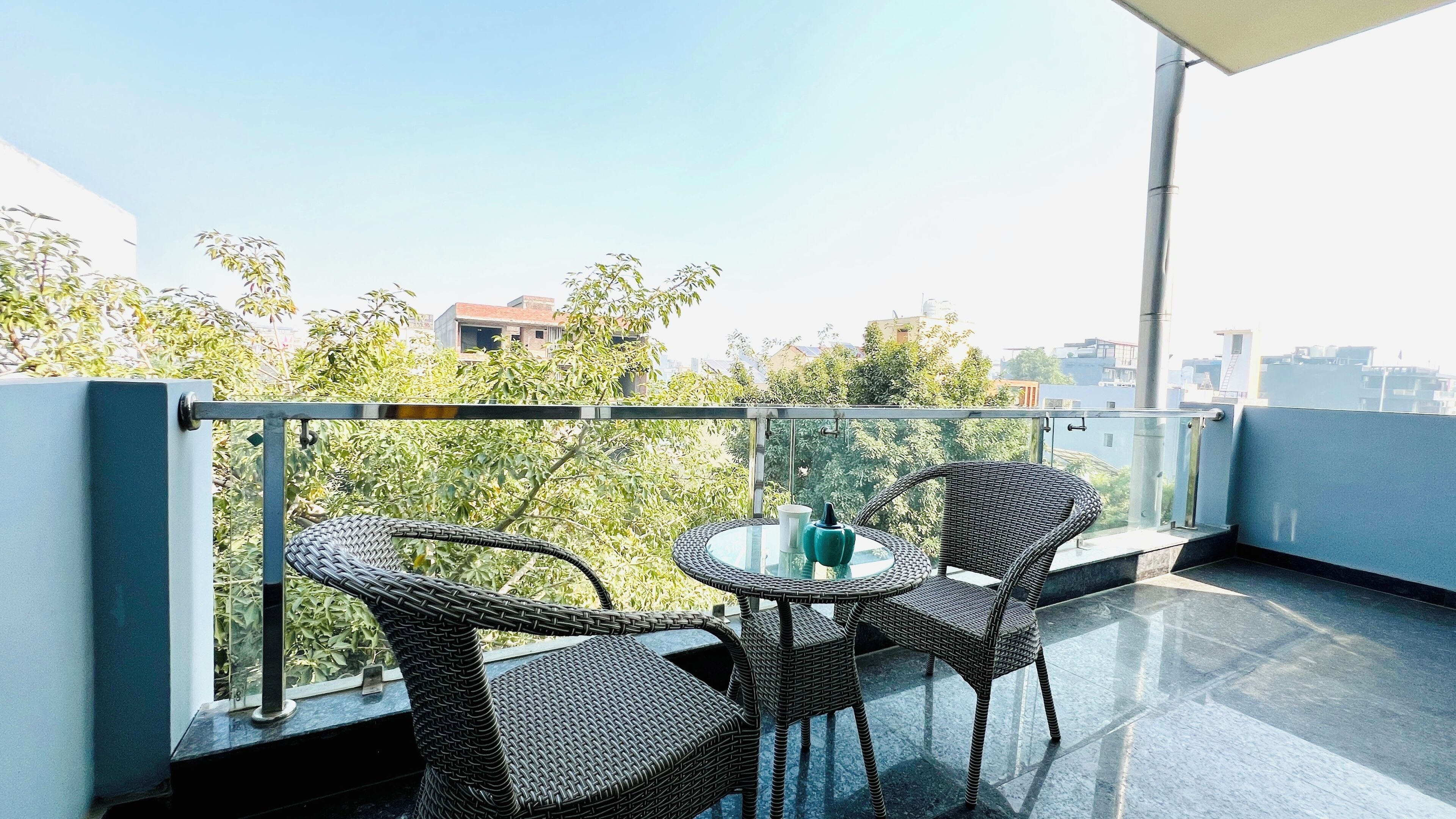 A balcony with wicker furniture and a glass table, overlooking a cityscape.