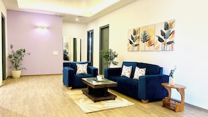 A living room with a blue sofa set, a coffee table, and a potted plant. - ZEN Medicity - Boutique Hotel Gurgaon (Gurugram)