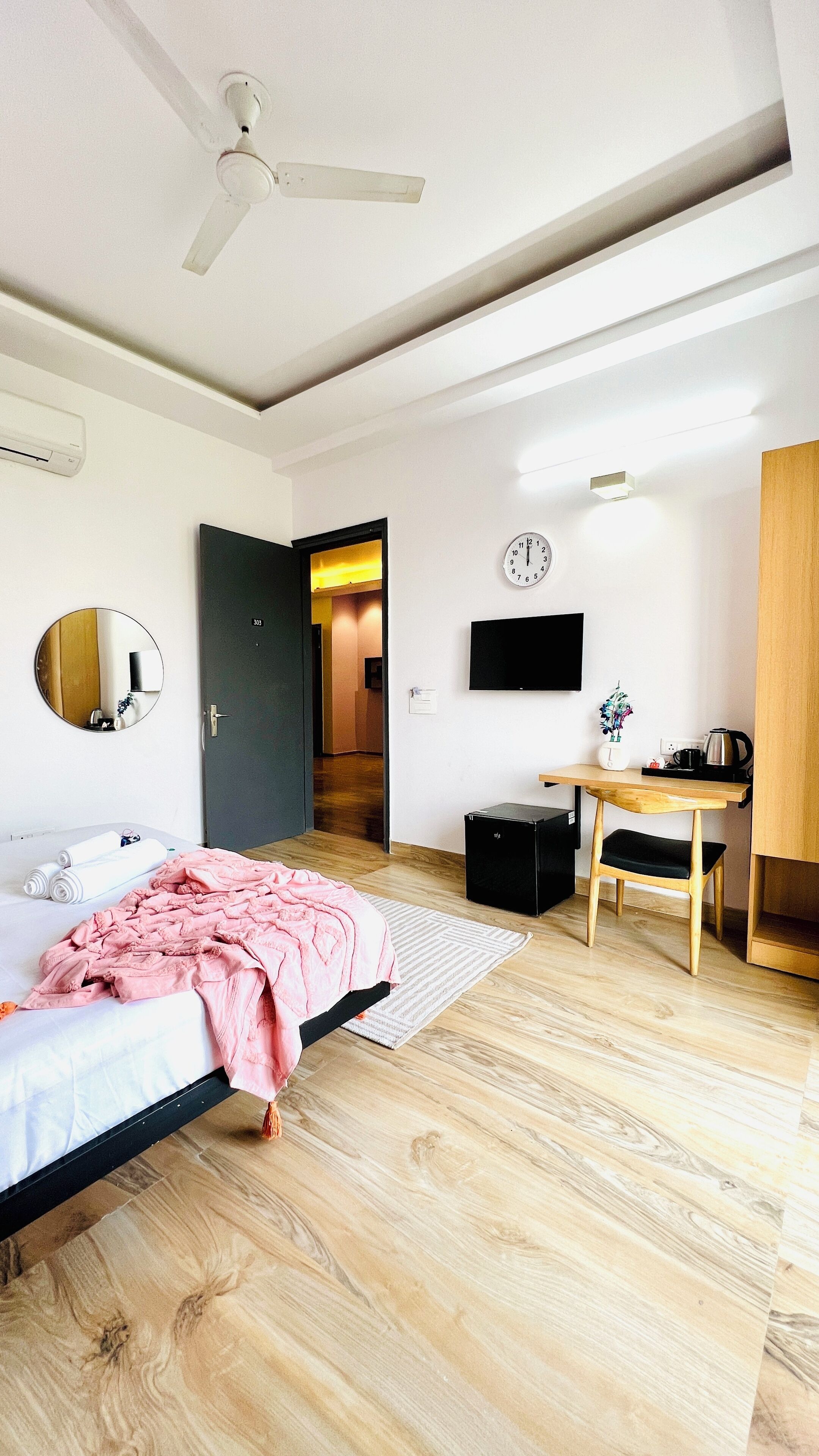 A modern bedroom with a bed, a desk, a chair, a mirror, a TV, and a ceiling fan.