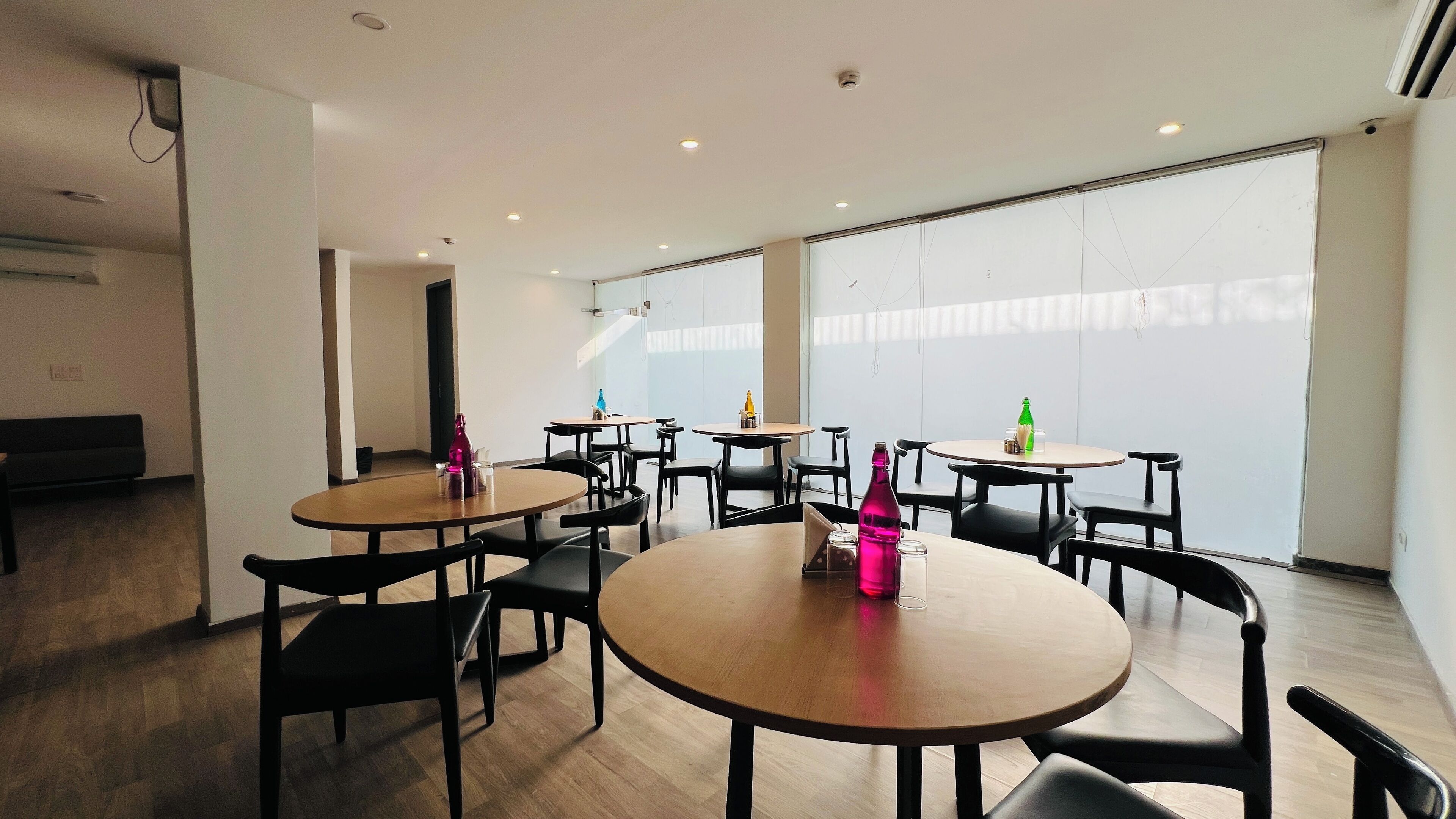 A modern indoor space with round tables and chairs, a bench, and large windows.