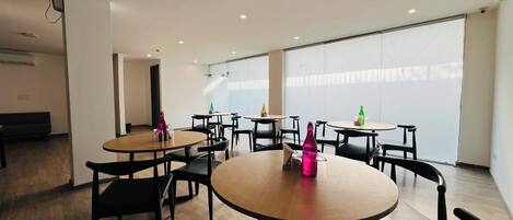 A modern indoor space with round tables and chairs, a bench, and large windows.
