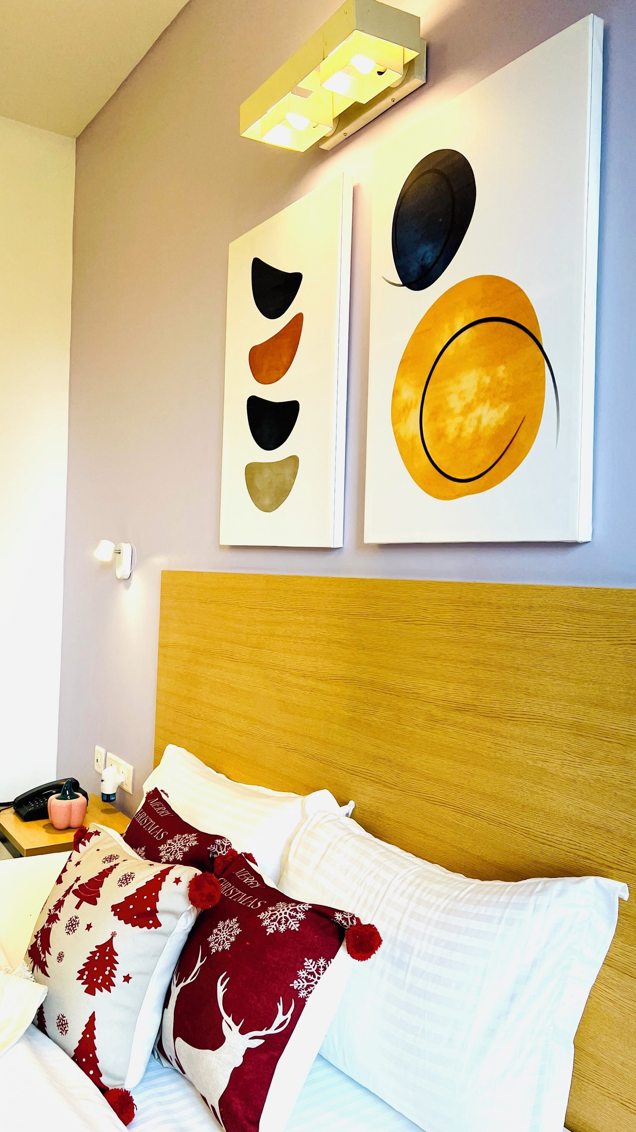 Une chambre d’hôtel avec une tête de lit en bois, un lit avec une literie blanche et rouge, et des œuvres d’art abstraites accrochées au mur.