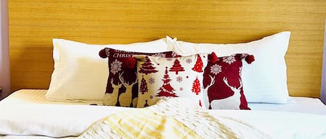 A neatly made bed with a white and maroon patterned pillow, a yellow and white striped blanket, and a tray with two mugs of coffee and a book titled "Adultery" by Paulo Coelho.
