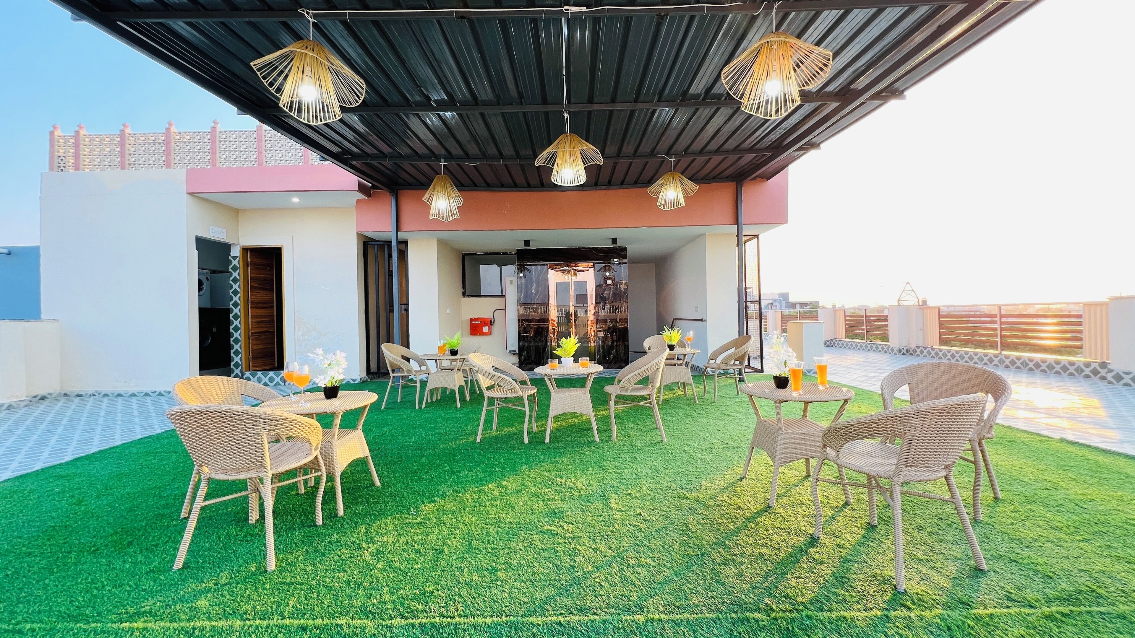 A rooftop terrace with artificial grass, wicker furniture, and hanging light fixtures.
