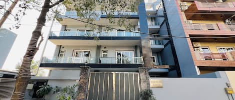 Un edificio residencial de varios pisos con entrada protegida por rejas, plantas en macetas y un balcón.