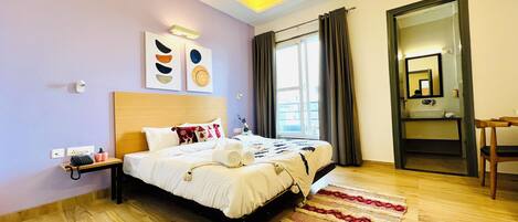 Habitación de hotel con cama, mesita de noche, lámpara, obra de arte, ventana con cortinas y espejo.