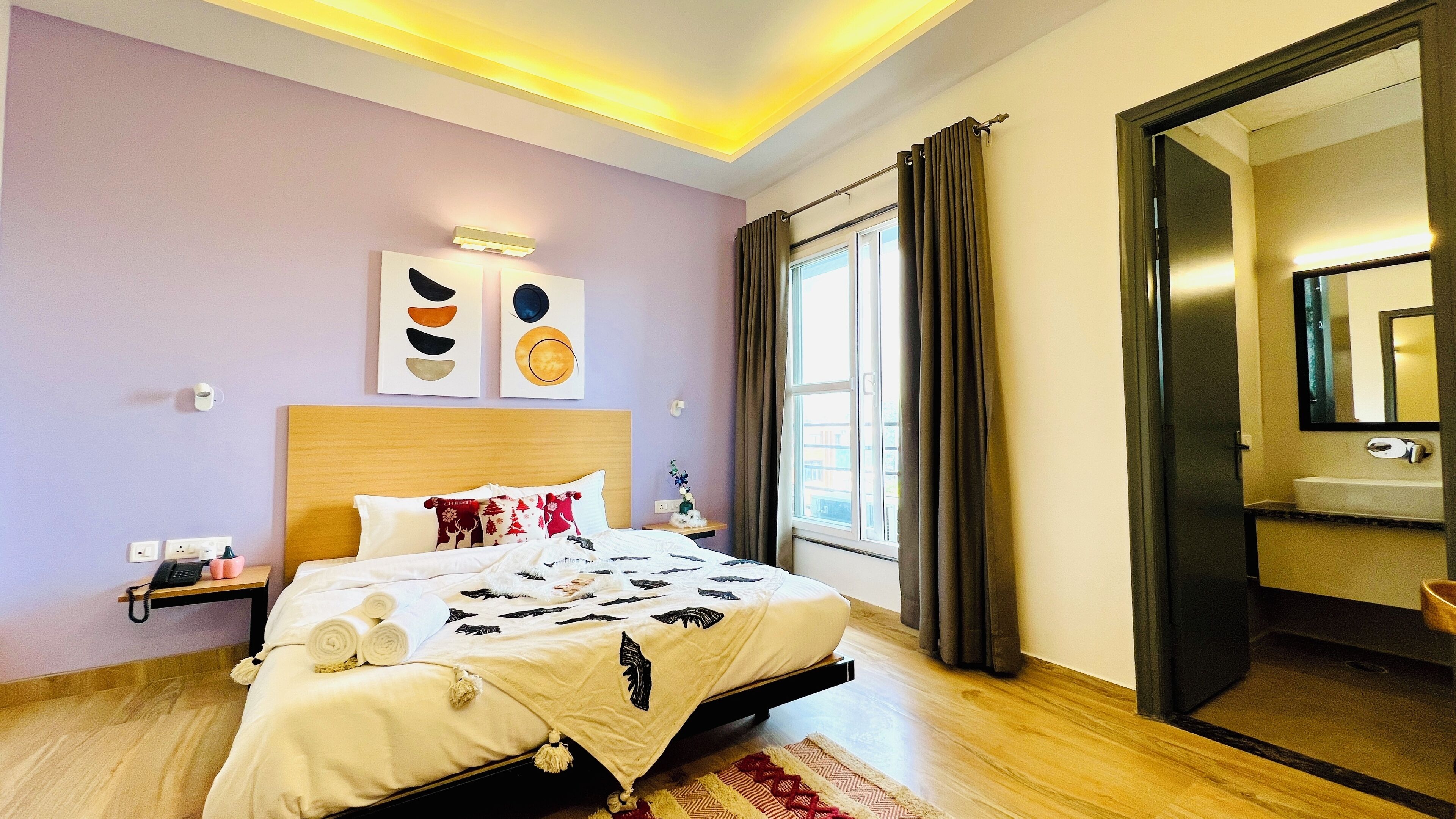 A modern hotel room with a large bed, a bedside table with a phone, a wall-mounted light, and a window with curtains.