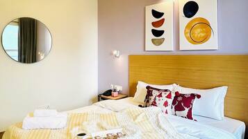 A hotel room with a bed, a round mirror, a wall-mounted air conditioner, and two wall art pieces.