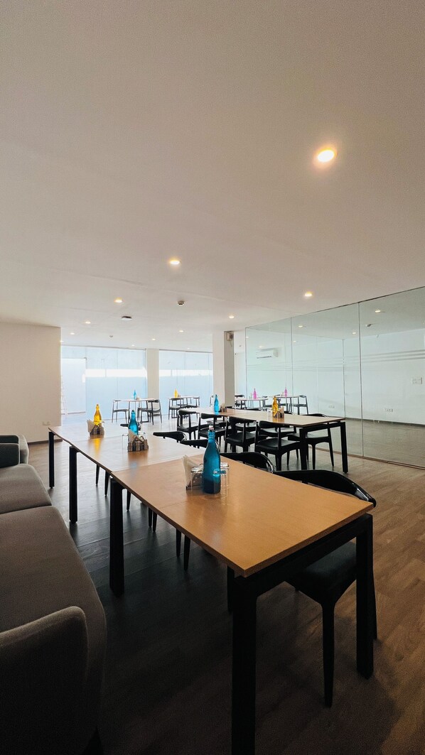 A spacious conference room with multiple tables and chairs, large windows, and a glass partition wall. - ZEN Medicity - Boutique Hotel Gurgaon (Gurugram)