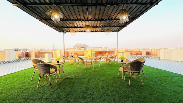 A rooftop terrace with artificial grass, wicker chairs, tables, and hanging lights. - ZEN Medicity - Boutique Hotel Gurgaon (Gurugram)