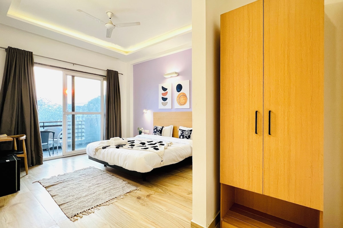 A bedroom with a bed, a desk, a chair, a wardrobe, and a view of the outdoors.
