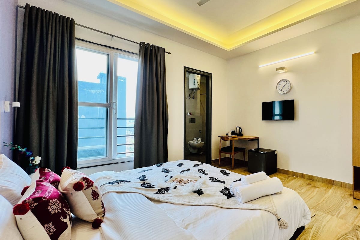 A hotel room with a bed, a desk, a television, a wardrobe, and a window with curtains.
