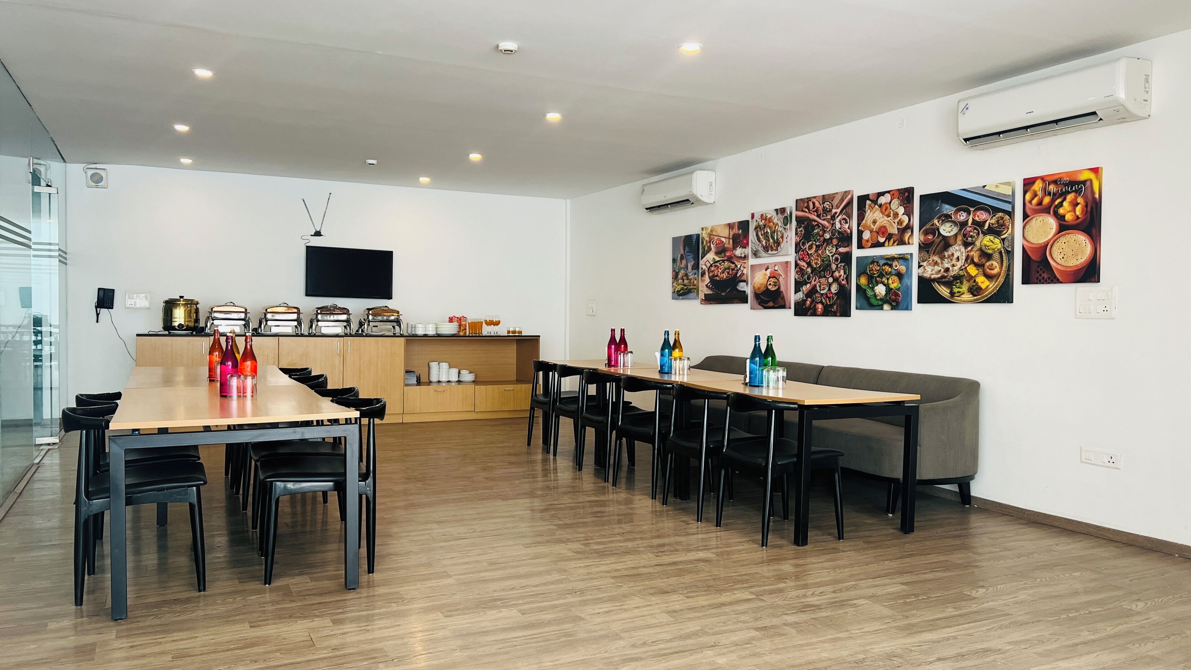 Un comedor moderno con mesas y sillas de madera, una zona de cocina con electrodomésticos y una pared decorada con motivos gastronómicos.