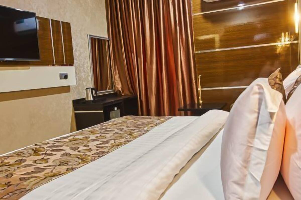 Quarto de hotel com uma cama grande, televisão de tela plana na parede, escrivaninha com chaleira e janela com cortinas.