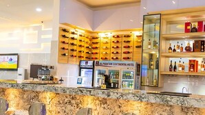 Un espace bar doté d’un comptoir en marbre, de plusieurs tabourets hauts et d’un mur entièrement recouvert de bouteilles de vin.