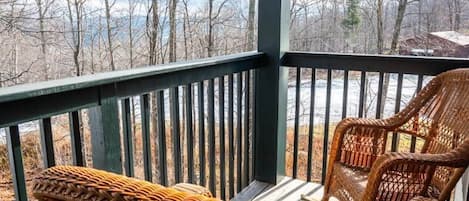A covered outdoor seating area with wicker chairs and a view of a forested landscape.