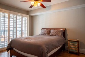 A bedroom with a bed, a ceiling fan, a window with blinds, and a nightstand.