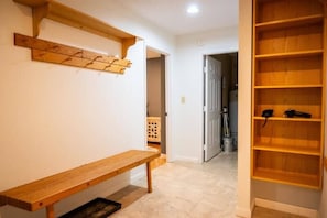 Un couloir avec un banc en bois, une étagère en bois et une porte donnant sur une autre pièce.