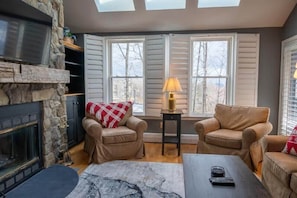 A cozy living room with a stone fireplace, two leather armchairs, a coffee table, and a lamp. - 3-BR Winterplace Ski-In/Out Okemo Condo w/ Loft (Ludlow)