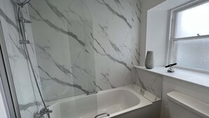 A modern bathroom with a marble wall, a bathtub, and a window. - St Cuthbert St Royal Suites (Kirkcudbright)
