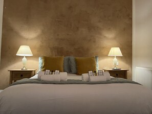 Cama bem arrumada com duas almofadas, duas mesas de cabeceira com abajures e uma parede com acabamento texturizado.