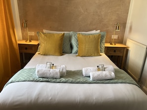 Cama bem arrumada com duas toalhas, um edredom verde e dois travesseiros em um quarto de hotel.