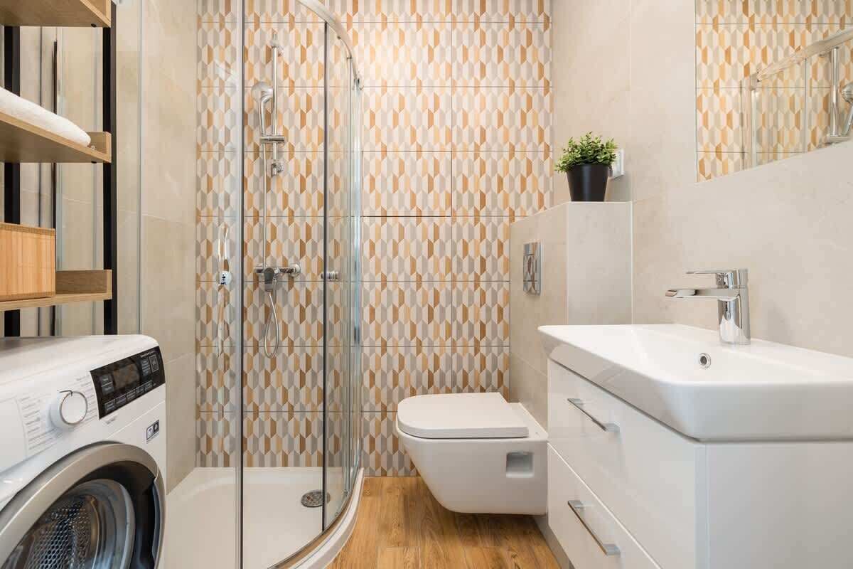 A modern bathroom with a glass shower enclosure, a built-in washing machine, and a white sink with a mirror above it.