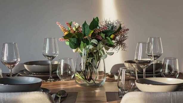 A dining table set with clear glassware, black and white plates, and a centerpiece of green foliage and dried branches. - Modern Apartment | Picturesque View of the Warta River (Poznan)