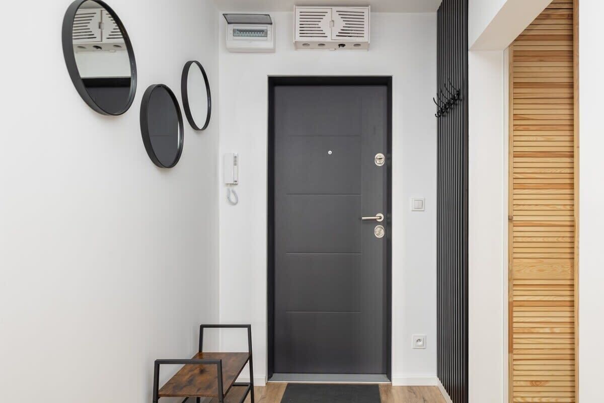 A modern entryway with a dark door, two wall-mounted mirrors, a small table, and a wooden panel on the right.