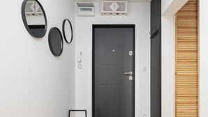 A modern entryway with a dark door, two wall-mounted mirrors, a small table, and a wooden panel on the right. - Modern Apartment | Picturesque View of the Warta River (Poznan)
