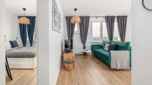 A modern living room with a green sofa, a small white table, and a wicker hanging light. - Modern Apartment | Picturesque View of the Warta River (Poznan)