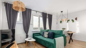 A modern living room with a green sofa, a flat-screen TV, a small round table, and a dining area with a wooden table and chairs. - Modern Apartment | Picturesque View of the Warta River (Poznan)