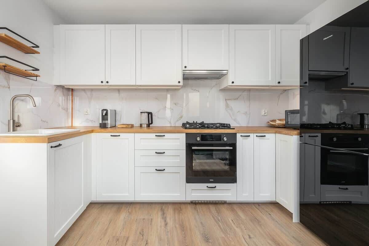 A modern kitchen with white cabinetry, a wooden countertop, a built-in oven, and a gas stove.