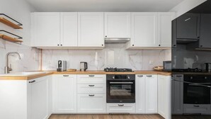 A modern kitchen with white cabinetry, a wooden countertop, a built-in oven, and a gas stove. - Modern Apartment | Picturesque View of the Warta River (Poznan)