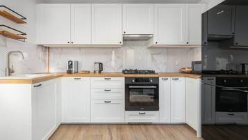 A modern kitchen with white cabinetry, a wooden countertop, a built-in oven, and a gas stove.