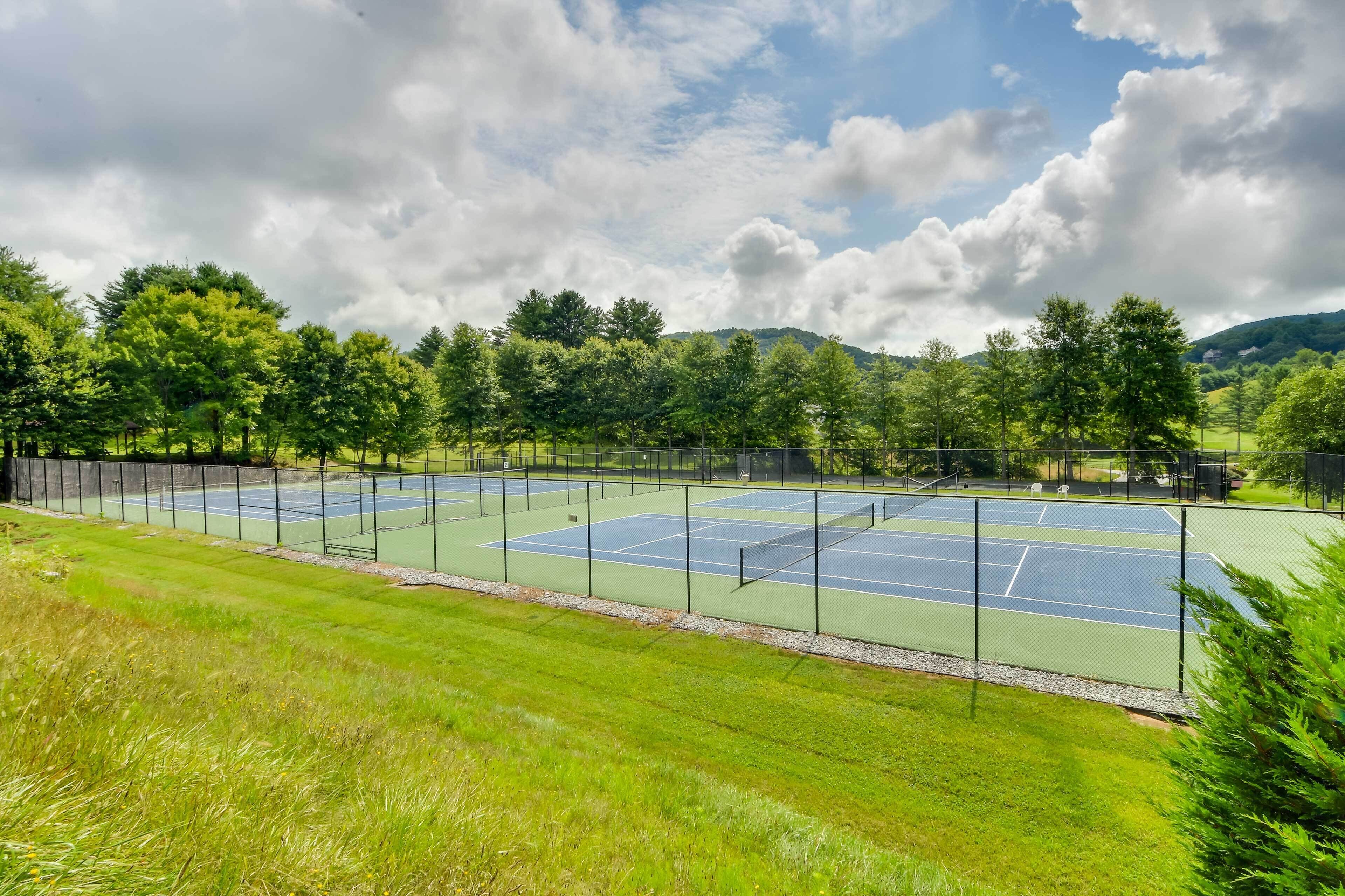 A tennis court surrounded by lush greenery and trees.
