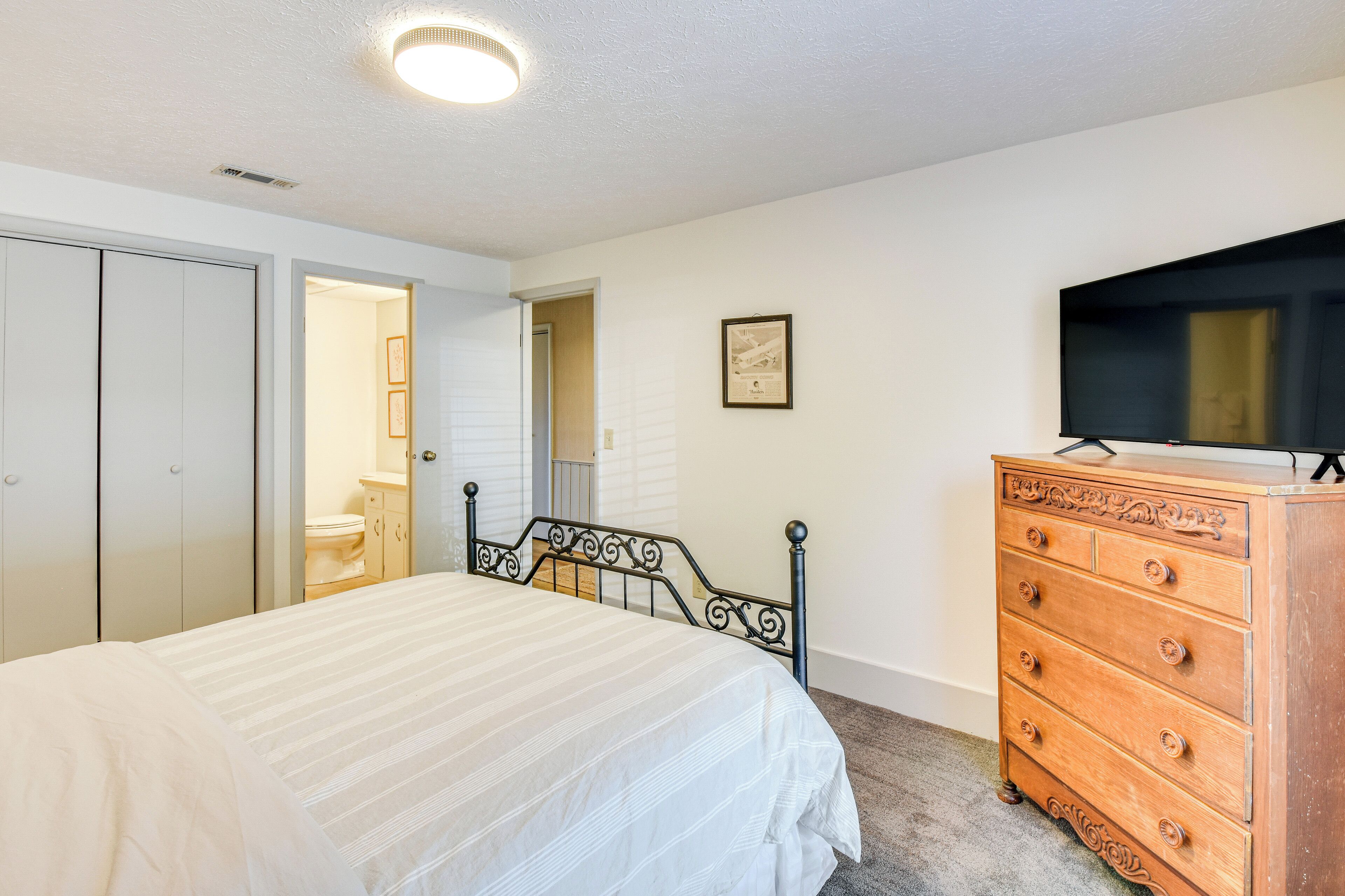 A bedroom with a bed, a dresser, a television, and a closet.