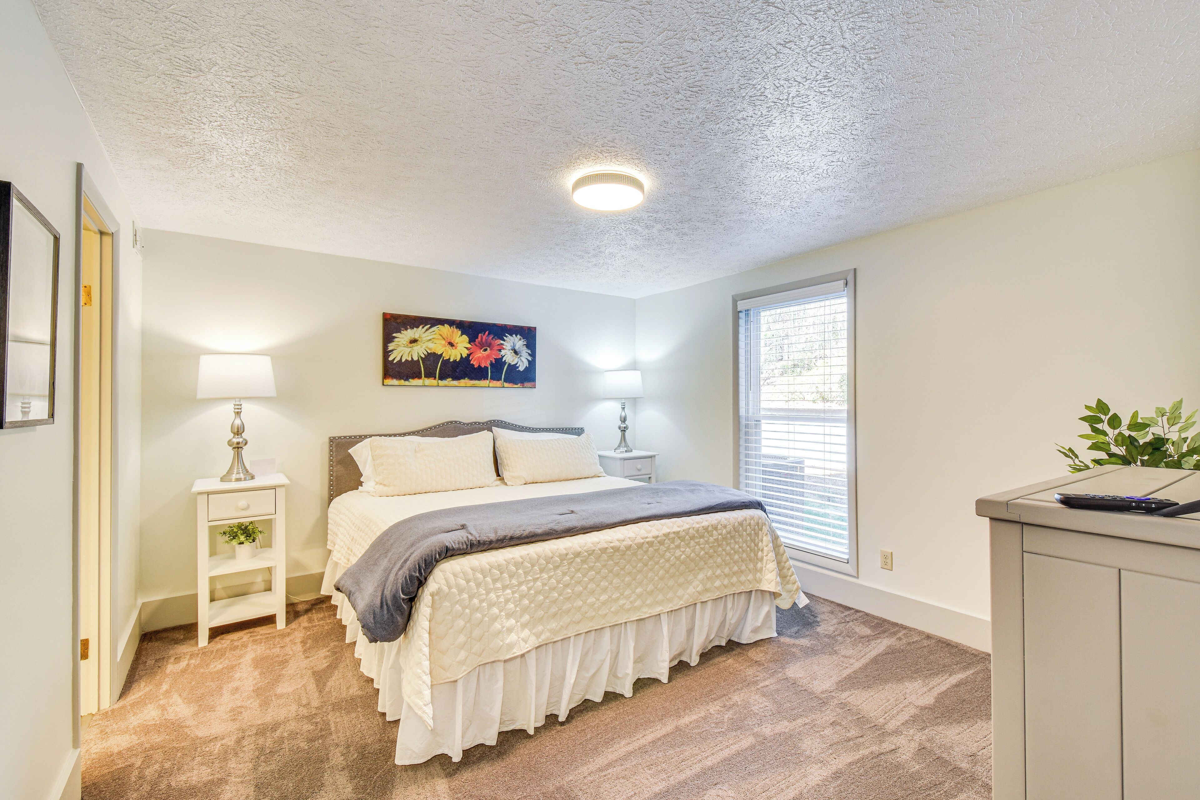A bedroom with a bed, bedside table, lamp, and a window with blinds.