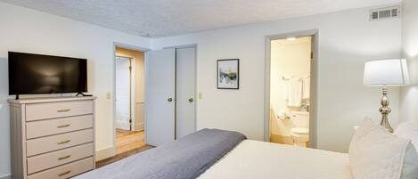 Un dormitorio con cama, cómoda, televisión y baño visible a través de una puerta abierta.
