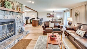 A spacious living room with a stone fireplace, leather sofas, and a dining area with a kitchen in the background.