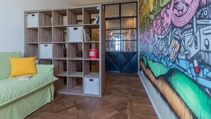 A room with a green sofa, a wooden bookshelf, and a colorful mural on the wall.