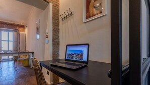A modern kitchen with a laptop on a counter, a dining area with chairs, and a brick wall.