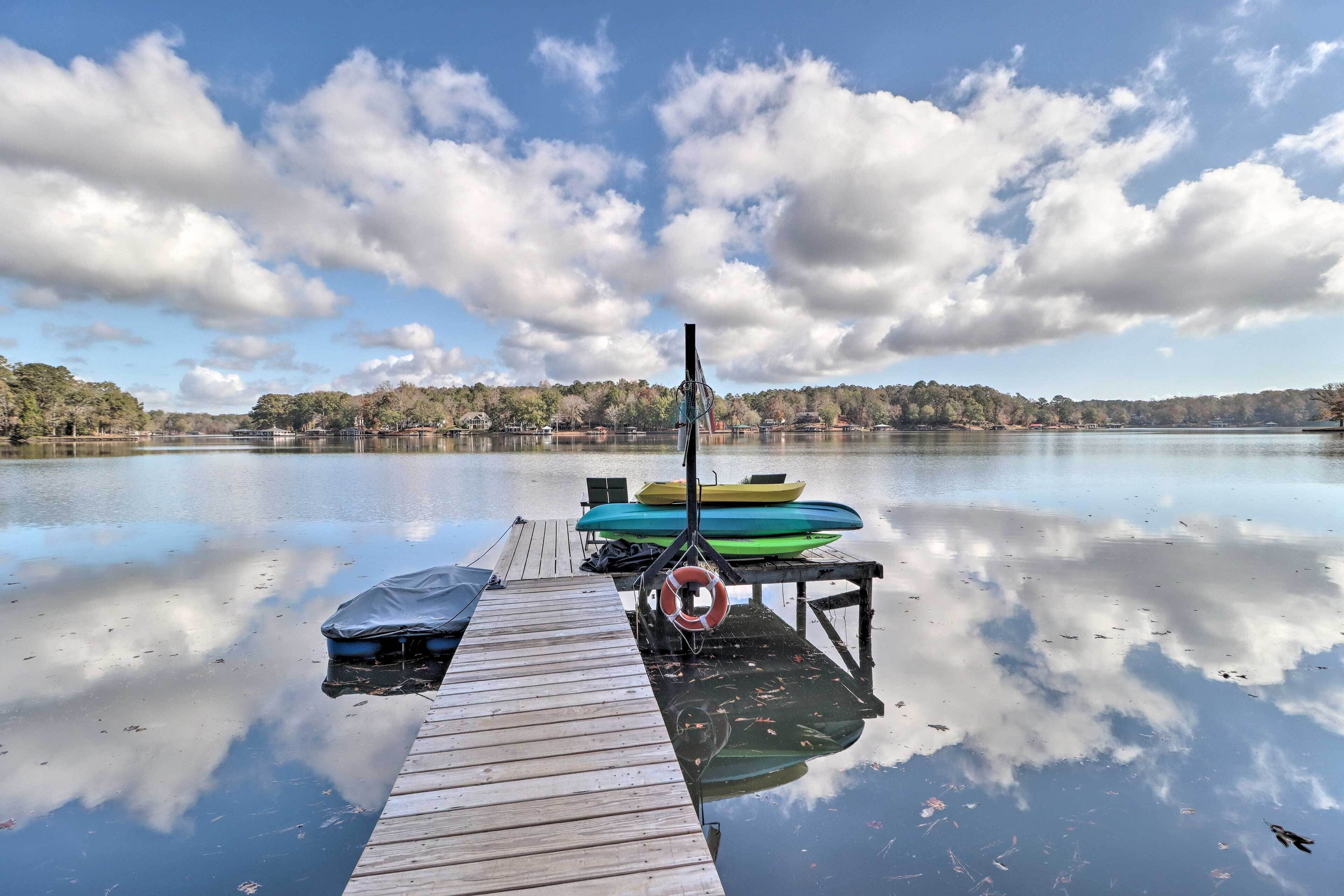 A wooden dock extending into calm water with a rowboat and a life preserver on it.