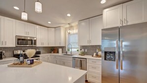 A modern kitchen with white cabinetry, stainless steel appliances, and pendant lighting.